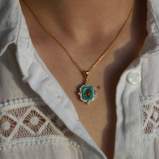 Close-up of a gold anklet with a blue stone on a person's ankle, wearing a light-colored lace garment.