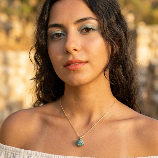 Woman wearing a necklace with a blue pendant against a blurred natural background