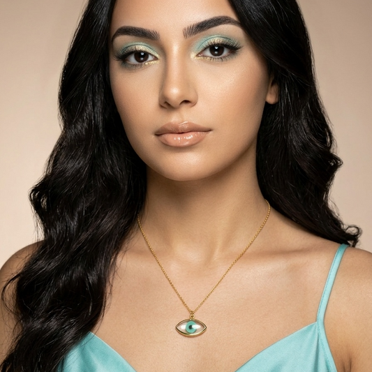Woman wearing a light blue top and gold necklace with an eye pendant against a beige background