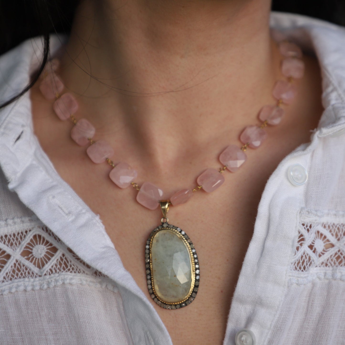 Necklace with a large pendant worn by a person in a white shirt.