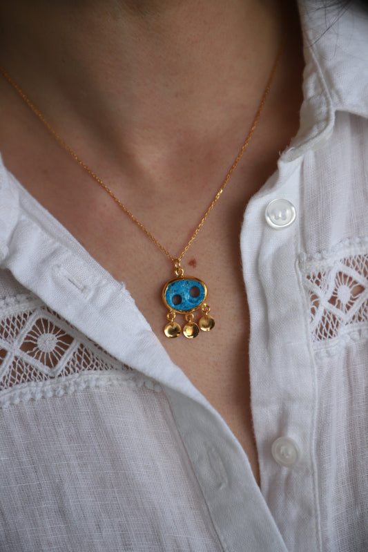 Gold anklet with a blue stone on a person's ankle against a white shirt background