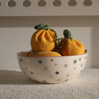 Knitted pumpkins in a bowl with star pattern on a textured surface