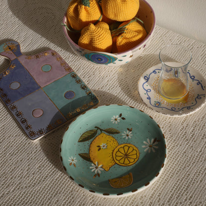Tea set with lemon-themed teacup, colorful teapot, and bowl of knitted yellow pumpkins on a textured surface.