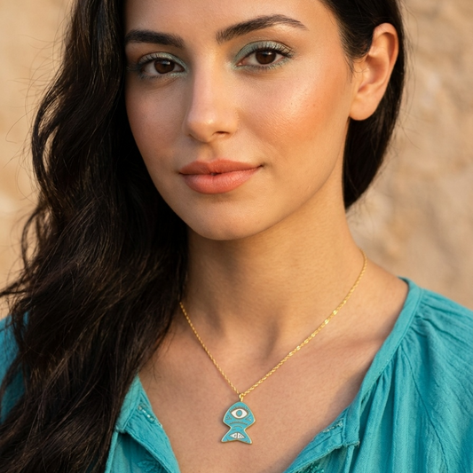 Woman wearing a turquoise top and gold necklace with a blue pendant against a beige background