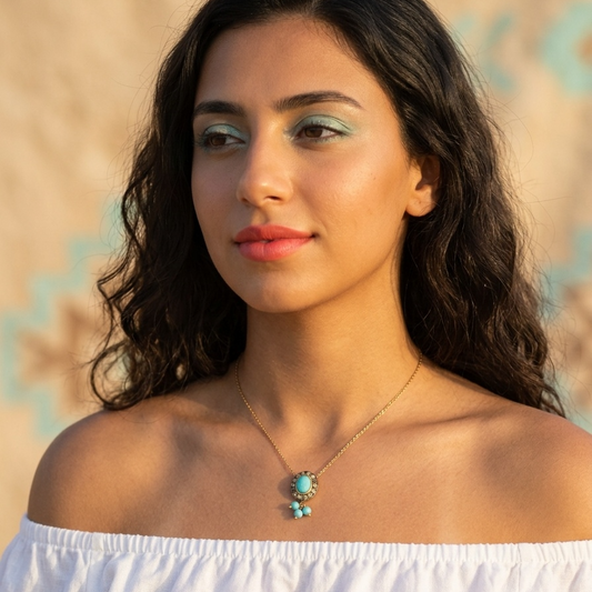 Woman wearing a white off-shoulder top with a necklace featuring turquoise stones against a blurred natural background.