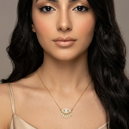 Woman wearing a gold necklace with an eye pendant against a neutral background