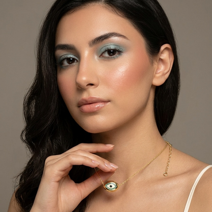 Woman wearing a gold necklace with an eye pendant against a neutral background