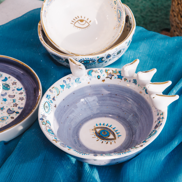 Stack of ceramic bowls with eye design on a blue fabric background